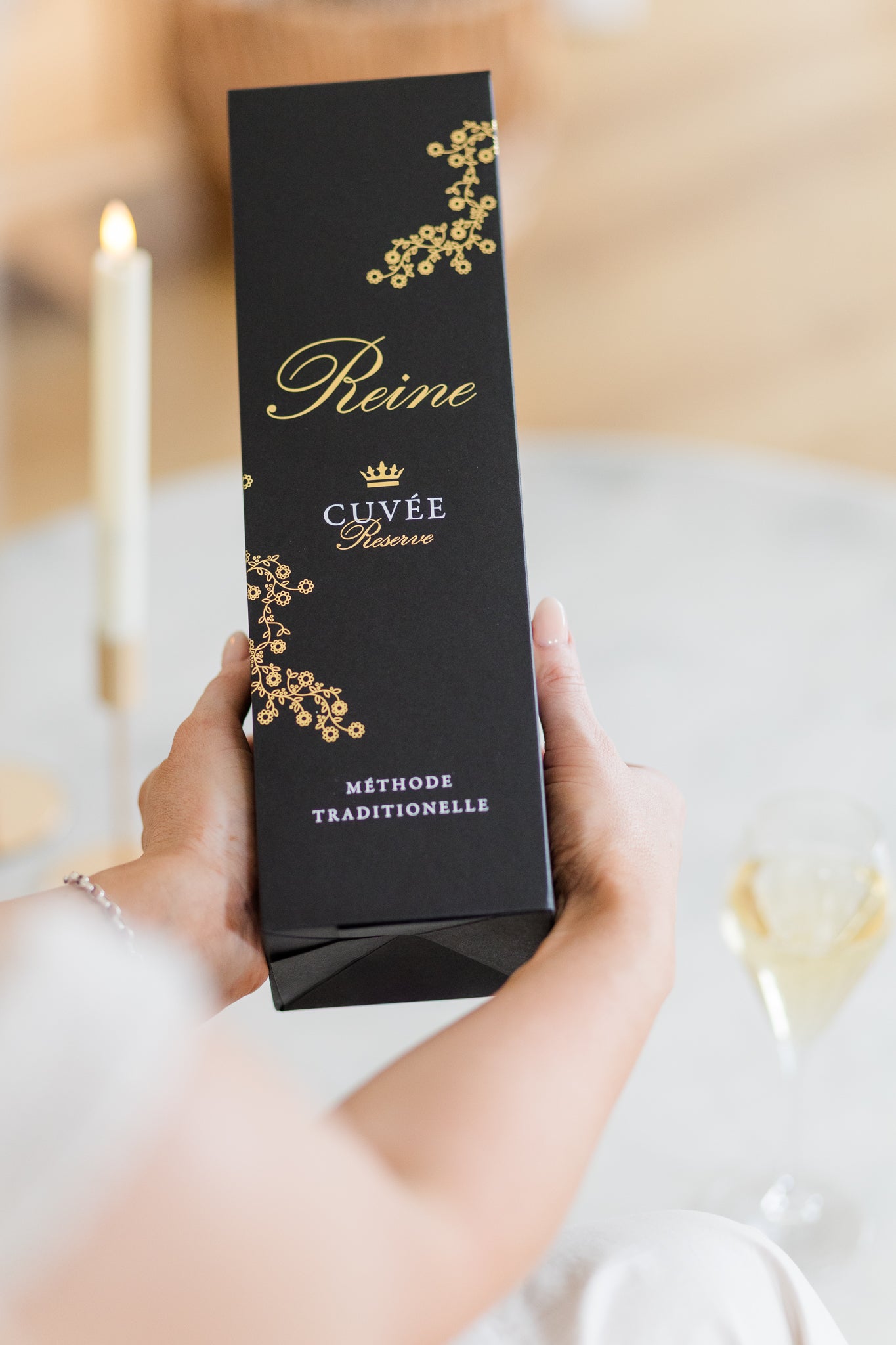 Women's hands holding a black Cuvee Reine gift box against a blurred background